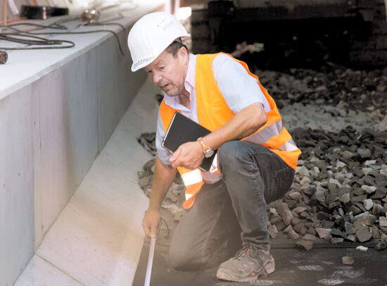 A Getzner employee in protective clothing measures vibration isolation next to a track bed. A Getzner employee in protective clothing measures vibration isolation next to a track bed.