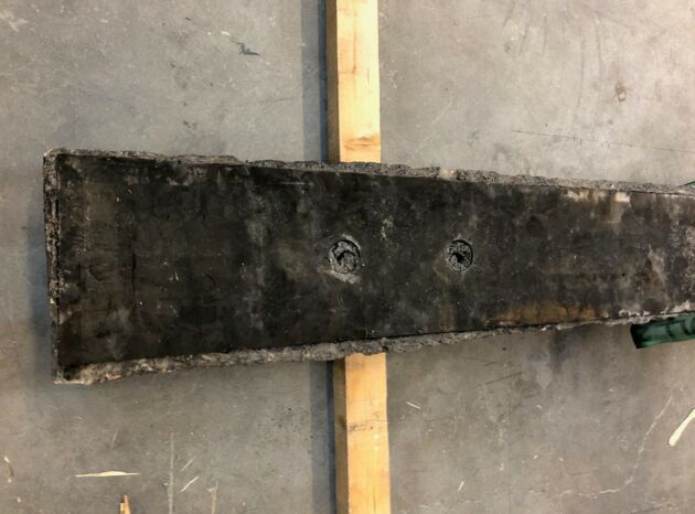 Eine schwarze DaQin Schwelle von unten, gelagert auf zwei Holzlatten auf einem Betonboden.