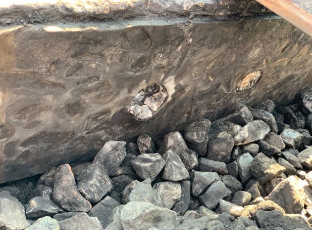 Wand mit Steinen und Vertiefungen, darüber Schottersteine, Baustellenmaterial.