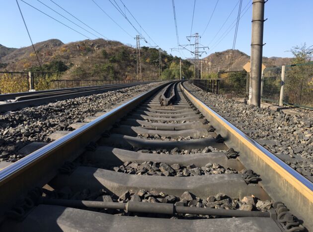 Eisenbahnstrecke biegt rechts ab, Schotterbett, Oberleitung, Bäume und Berge.