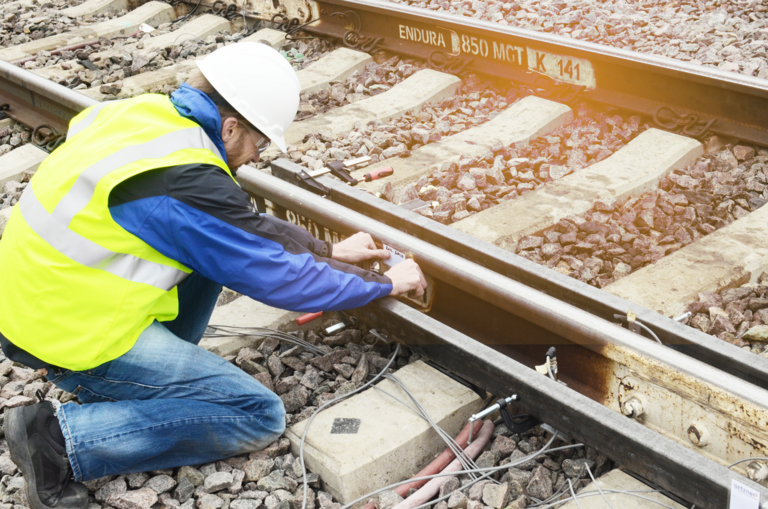 Worker installing measuring devices for vibration analysis on railway tracks.