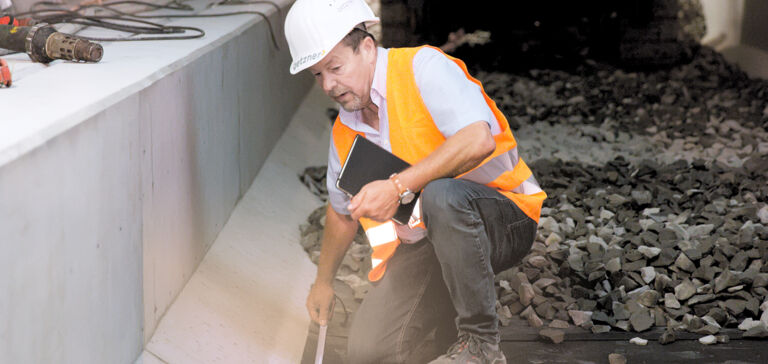 A Getzner employee in protective clothing measures vibration isolation next to a track bed. A Getzner employee in protective clothing measures vibration isolation next to a track bed.