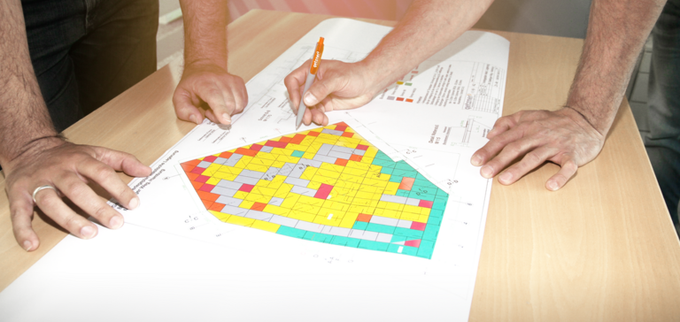 A close-up of people leaning over a construction blueprint and reviewing installation plans. A close-up of people leaning over a construction blueprint and reviewing installation plans.