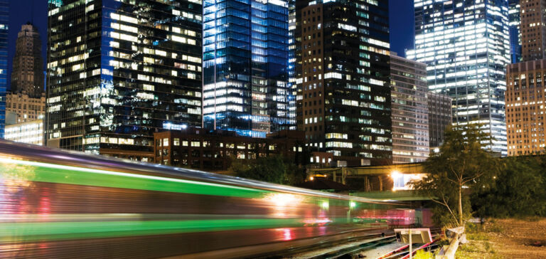 Commuter train at night in front of skyscrapers. Example of structure-borne noise insulation.